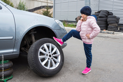  A small child standing in front of his broken car looking at the wheel.
