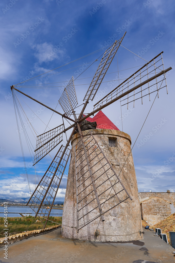 Old stone wind powered mill on the roof of old traditional seasalt manufacture in italian island Sicily cluse to city Trapani and Erice. Ancient technology still in use for top quality salt production