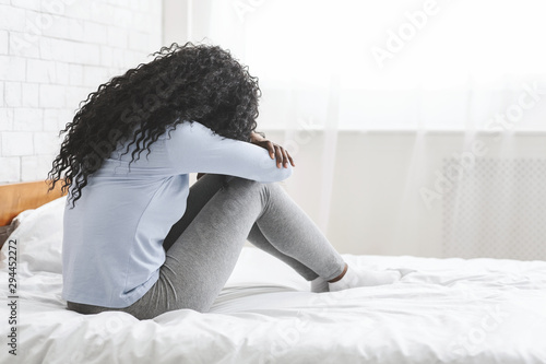 Back view of lonely young woman sitting on bed