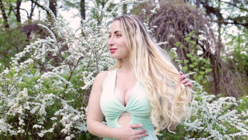 Young beautiful blonde woman admires the blossoming garden among the trees. Young beautiful blonde woman admires the blossoming garden among the trees.