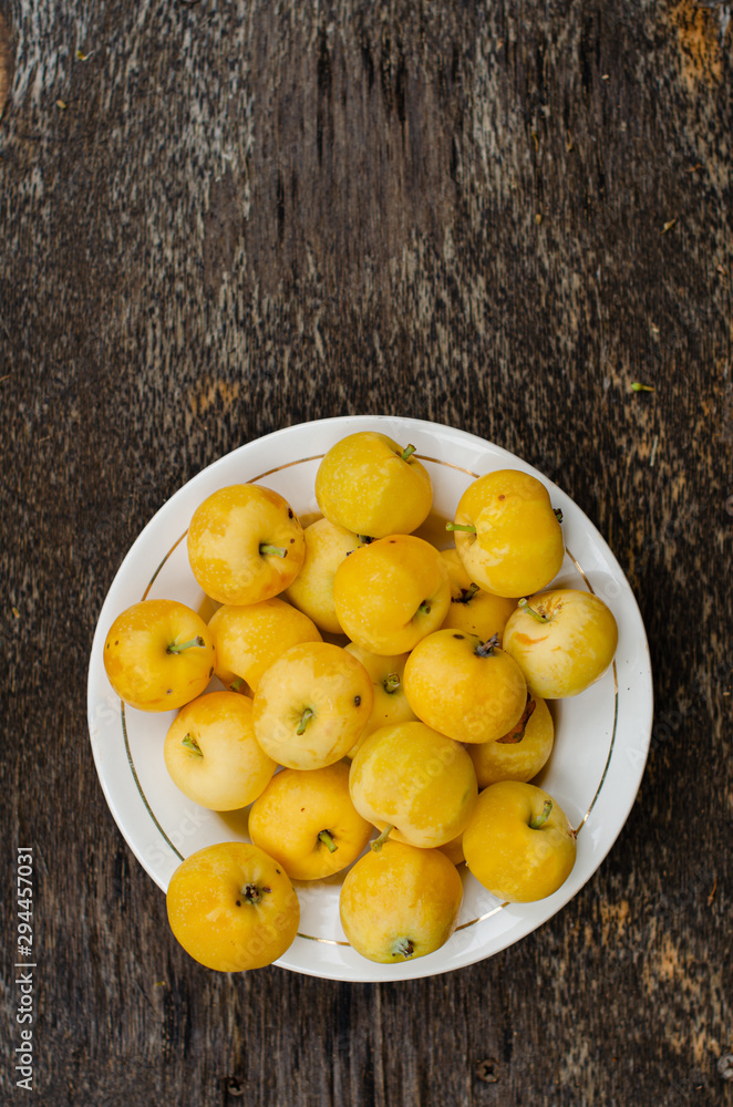 Little yellow apples on the plate on old wooden background