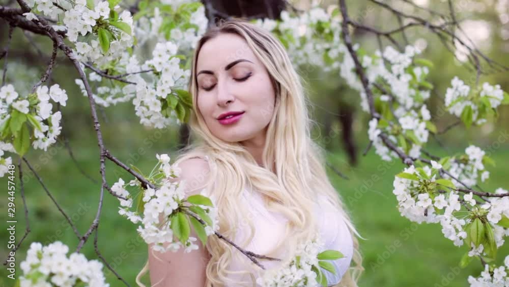 Beautiful young woman stands near a flowering tree in the garden. Beautiful young woman stands near a flowering tree in the garden.