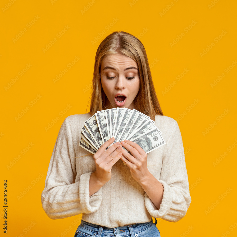 Shocked young girl holding fan of dollar banknotes Shocked young girl holding fan of dollar banknotes
