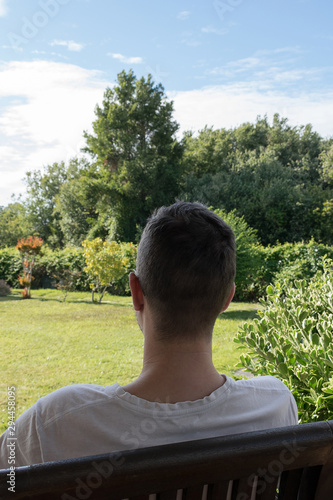 Rear view of a boy sitting on a chair in the garden on a sunny day