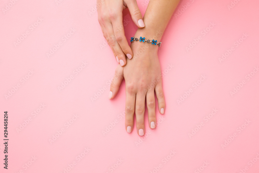 Blue flower bracelet on woman's wrist. Pastel pink background. Care about hand skin and nails. Closeup. - obrazy, fototapety, plakaty 