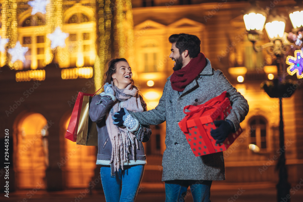 Young couple in the city centre with holiday's brights in background. Man presenting gift to woman. Young couple in the city centre with holiday's brights in background. Man presenting gift to woman.