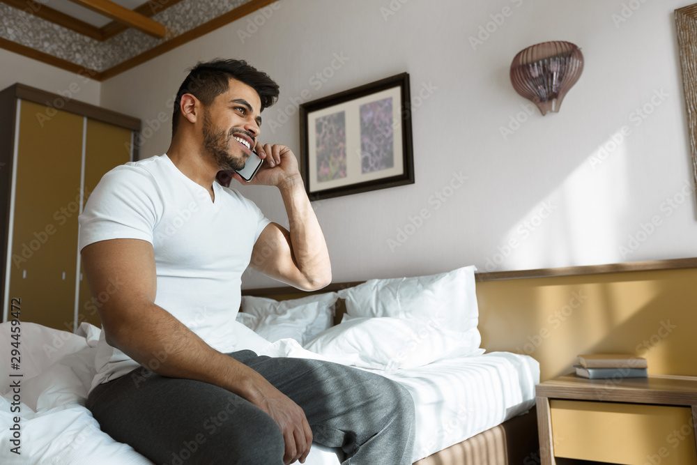 Cheerful guy talking on phone in bed