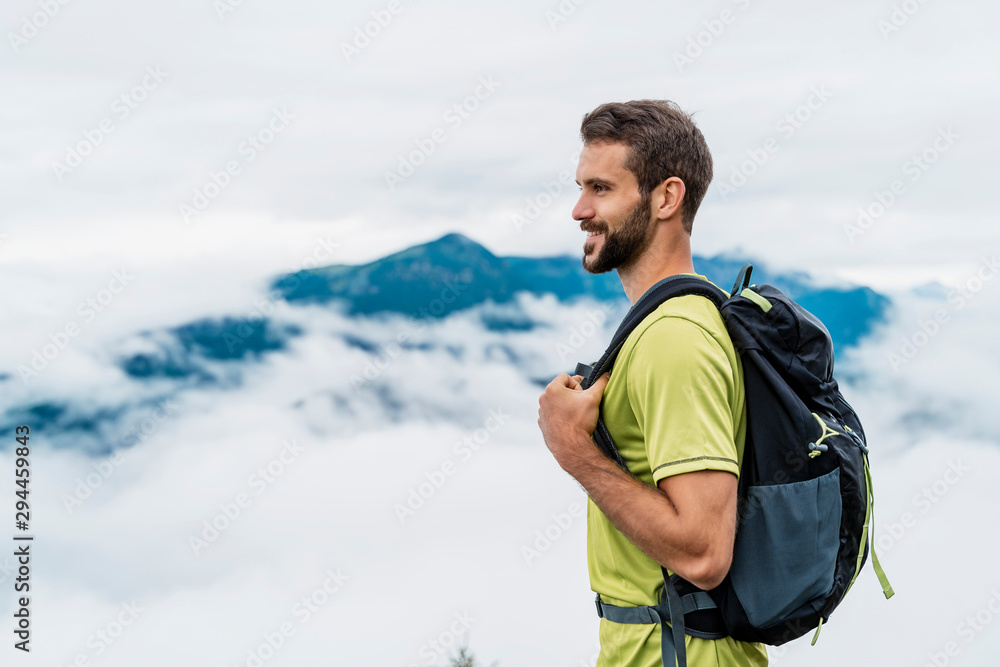 Smiling young man on a hiking trip in the mountains looking at view, Herzogstand, Bavaria, Germany Smiling young man on a hiking trip in the mountains looking at view, Herzogstand, Bavaria, Germany