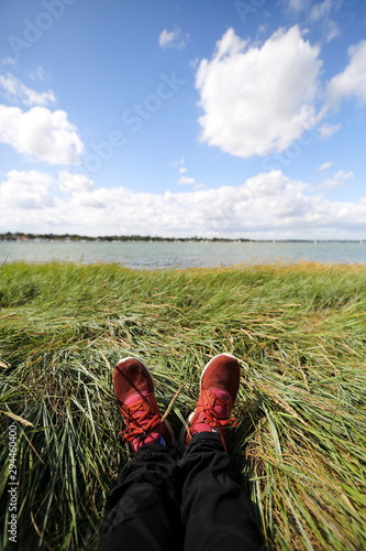 First person view on a males legs sitting on the floor by a river on a bright summers day