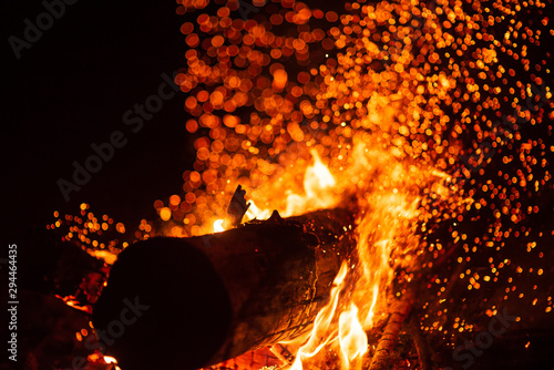 Beautiful abstract background on the theme of fire, light and life. Burning red hot sparks fly from large fire in the night sky. Burning embers glowing flying over black background.