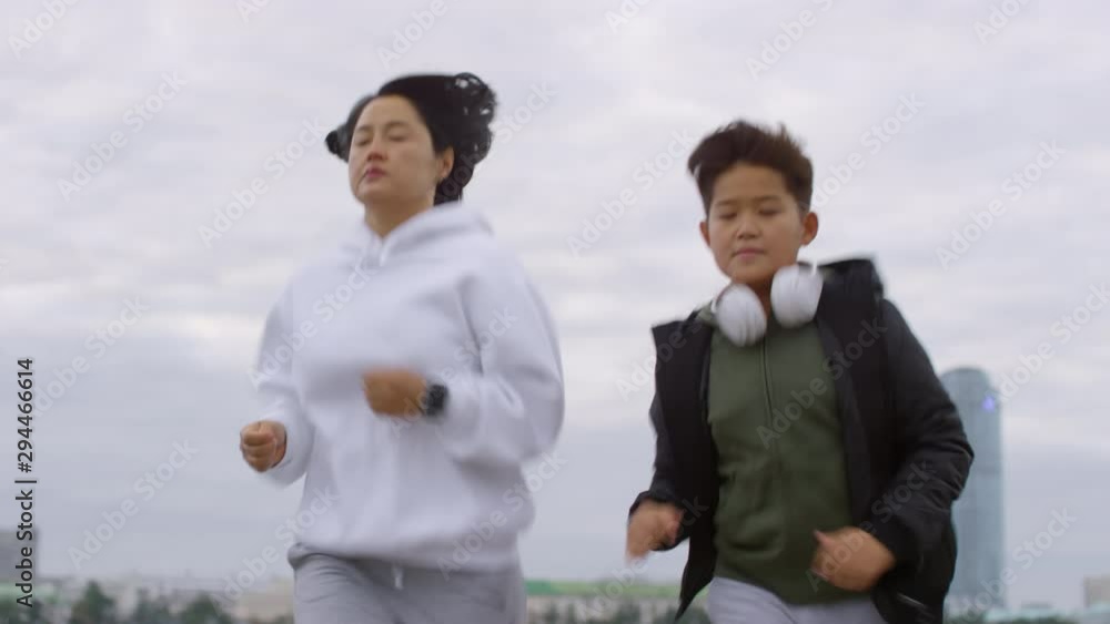 Low angle shot of Asian mother and young son running together in city while training in the morning Low angle shot of Asian mother and young son running together in city while training in the morning