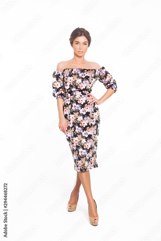 Beautiful elegant young woman with fashion hairstyle and makeup posing on a white background on high heels isolated in a floral dress. Free space for text mockup Beautiful elegant young woman with fashion hairstyle and makeup posing on a white background on high heels isolated in a floral dress. Free space for text mockup