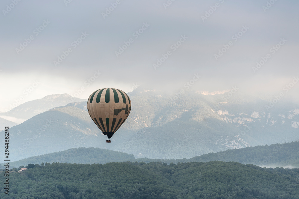 A hot air balloon flies over a sea of clouds in the region of La Garrotxa, in Girona (Spain) at dawn. - obrazy, fototapety, plakaty 