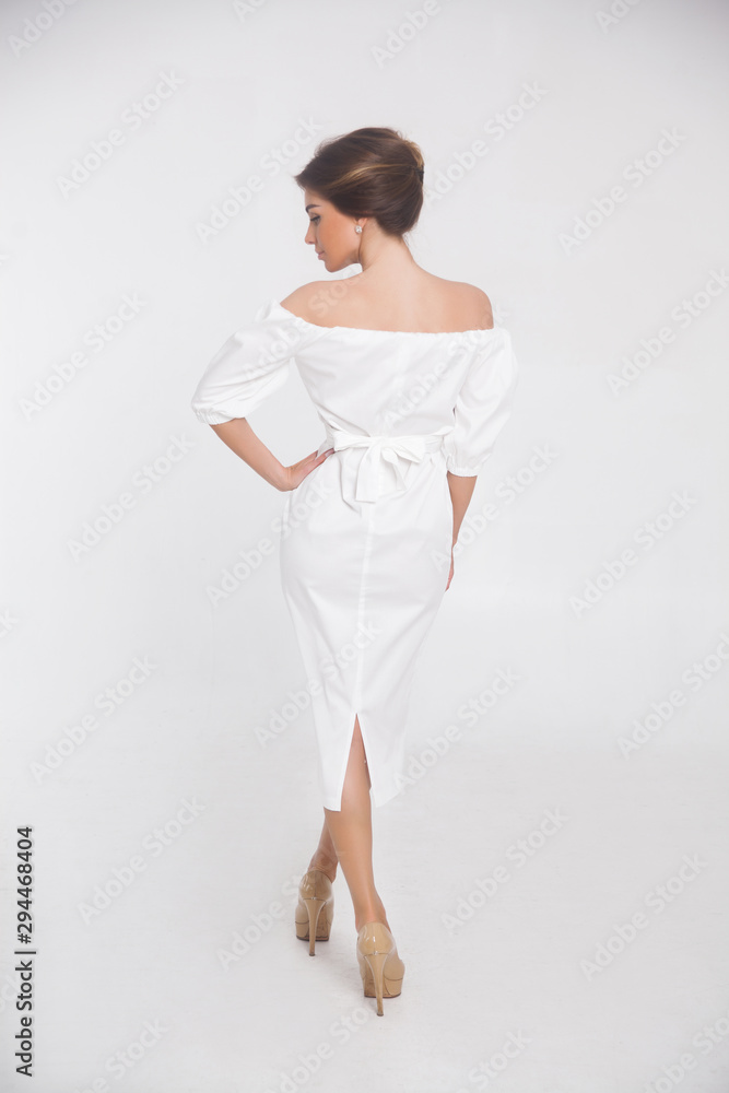 Beautiful elegant young woman with fashion hairstyle and makeup posing on a white background on high heels isolated in a white dress back view. Free space for text mockup Beautiful elegant young woman with fashion hairstyle and makeup posing on a white background on high heels isolated in a white dress back view. Free space for text mockup