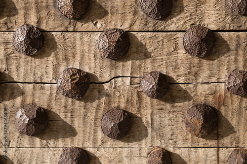 Heavy wooden medieval door with rusty metal studs - detail. Historical Luhike Jalg gate in Tallinn, Estonia old town. Strong side lighting reveals natural wood texture. photo