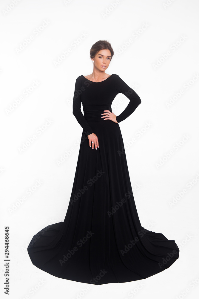 Beautiful elegant young woman with fashion hairstyle and makeup posing on a white background on high heels isolated in a black long evening dress. Free space for text mockup