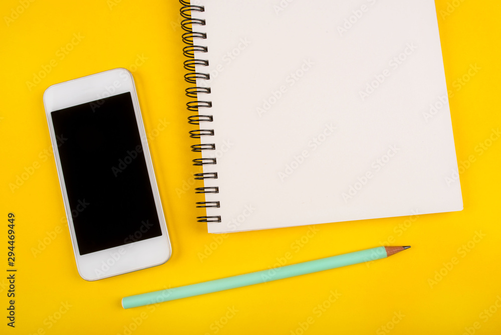 Empty notebook, pencil and phone on yellow background, top view. Empty notebook, pencil and phone on yellow background, top view.