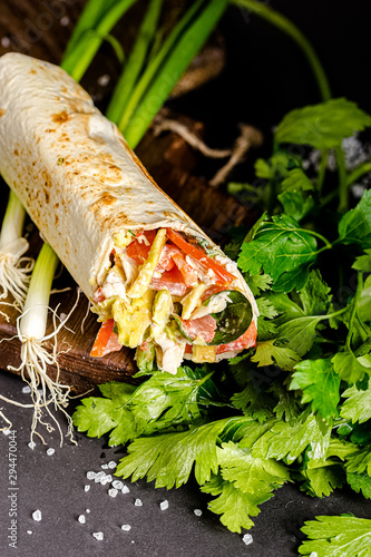 Freshroll shawarma with chicken meat, avocado, standing and lying in a paper container, cutting board with burlap, shot from above and side view, isolated on a black dark background photo