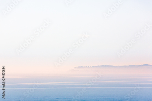 Minimalist landscape scene of Sandwich Bay, Kent on a misty but bright summer morning. The town of Deal peninsular can just be seen through the mist and there is a soft glow of sunrise. photo