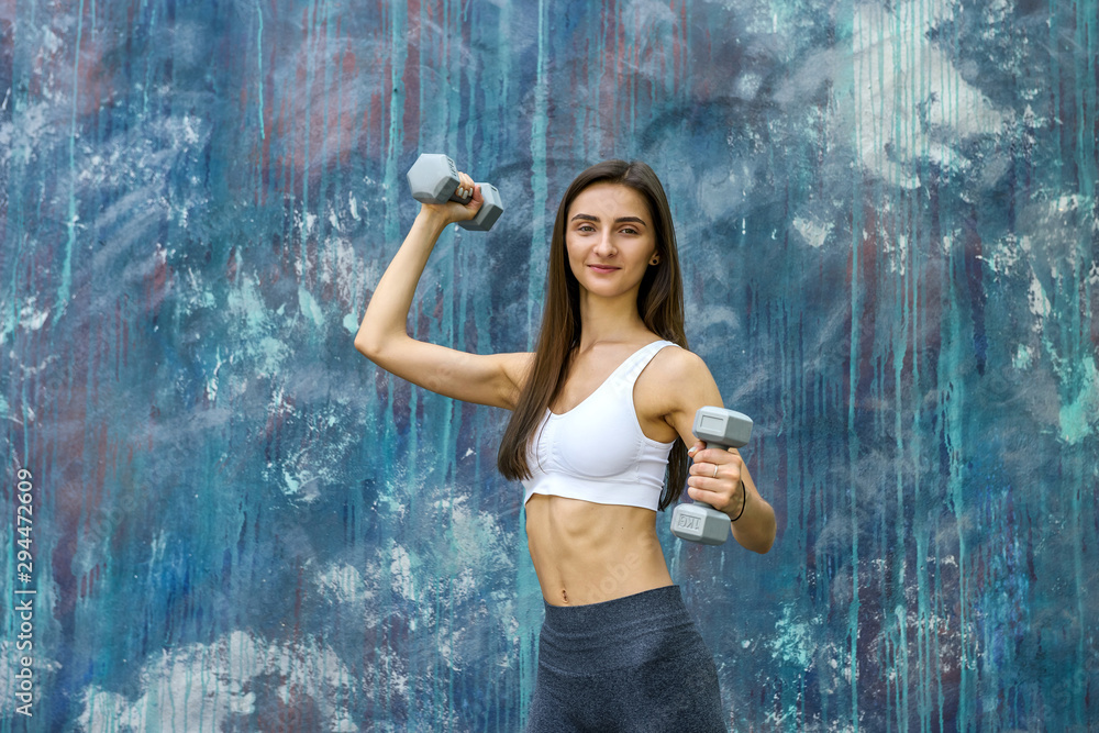 Obraz premium Woman doing fitness exercises. Young woman with dumbells posing outdoors