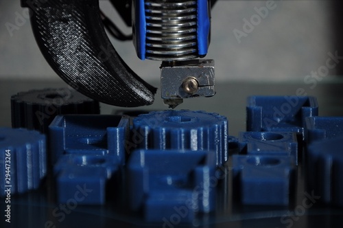 Close-up of 3D printed parts made of blue plastic and the print head of the printer