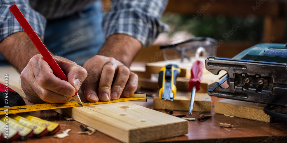 Adult carpenter craftsman with a pencil and the carpenter's square trace the cutting line on a wooden table. Construction industry, housework do it yourself. Stock photography. Adult carpenter craftsman with a pencil and the carpenter's square trace the cutting line on a wooden table. Construction industry, housework do it yourself. Stock photography.