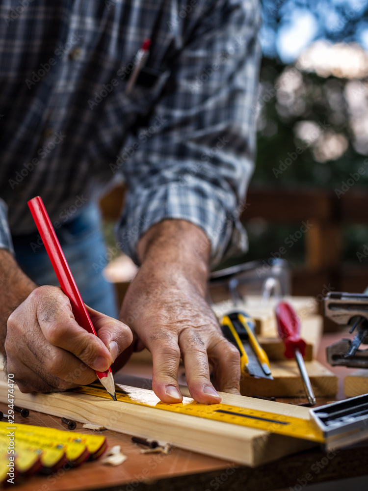 Adult carpenter craftsman with a pencil and the carpenter's square trace the cutting line on a wooden table. Construction industry, housework do it yourself. Stock photography. Adult carpenter craftsman with a pencil and the carpenter's square trace the cutting line on a wooden table. Construction industry, housework do it yourself. Stock photography.