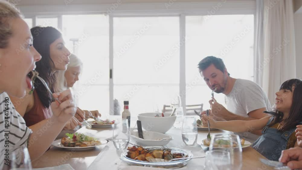 Multi Generation Family Sitting Around Table At Home Eating Meal Together