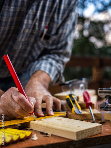 Adult carpenter craftsman with a pencil and the carpenter's square trace the cutting line on a wooden table. Construction industry, housework do it yourself. Stock photography.