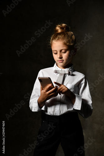 Little female caucasian model posing in school uniform on a gray concrete studio background. photo