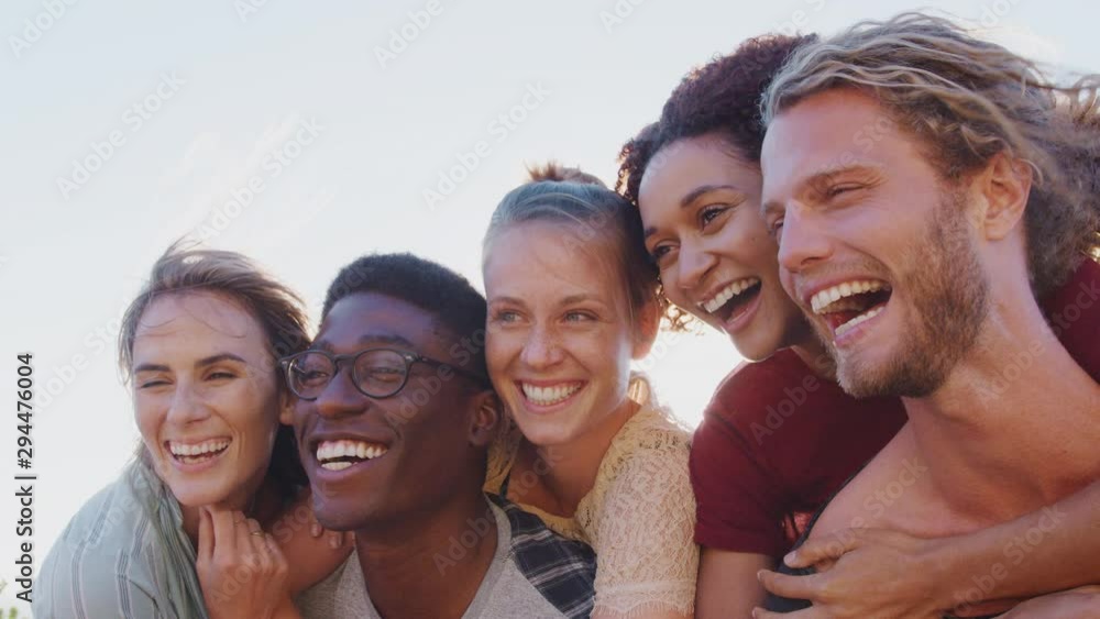 Men Giving Women Piggybacks As Group Of Friends Smile Against Flaring Sun Men Giving Women Piggybacks As Group Of Friends Smile Against Flaring Sun