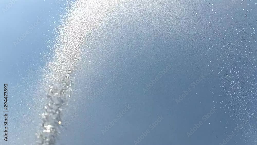 Against the background of the blue sky with white clouds, a jet of water in slow motion, sprinkles drops around. Background Against the background of the blue sky with white clouds, a jet of water in slow motion, sprinkles drops around. Background