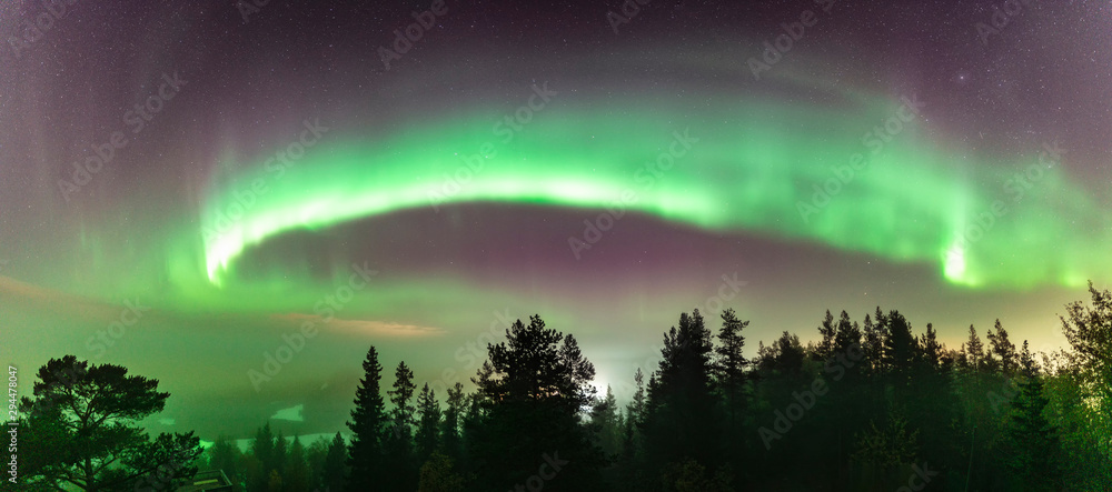 Northern Lights at partly clear skies with thick fog shines above Swedish foggy forest landscape in mountains, green northern lights belt curved above horizon line, Northern Sweden, Scandinavia