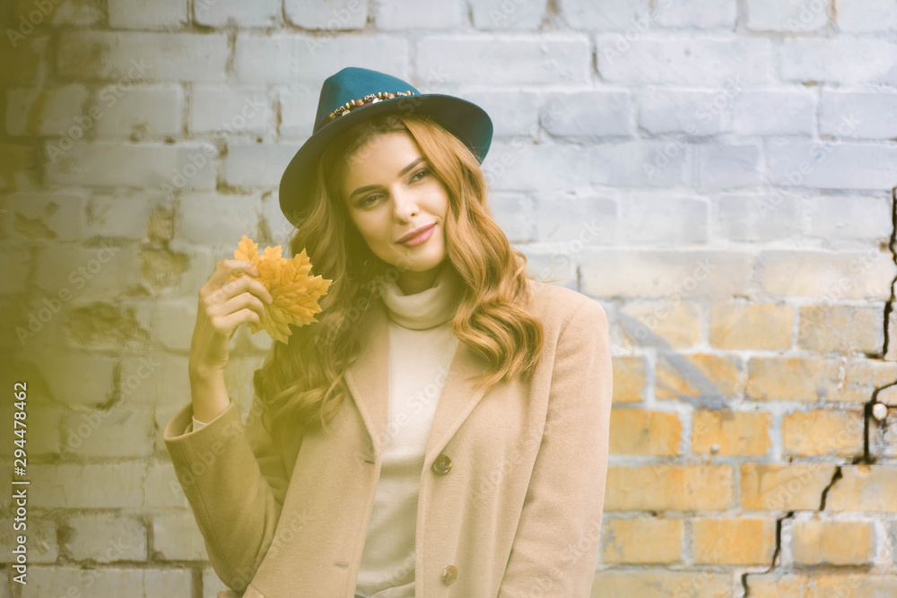 attractive woman in blue hat looking at camera and holding yellow leaves
