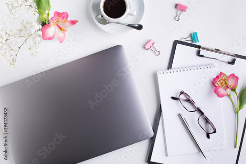 Female workspace with tablet, ballpoint pen, glasses, laptop, flowers and a cup of black coffee, top view