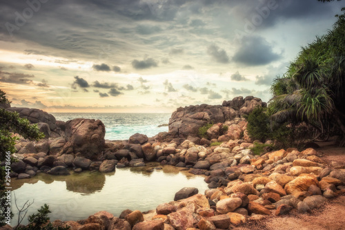 Beach rocks lagoon tropical landscape with palm trees and round stones with sunset sky vibrant colors in Sri Lanka
