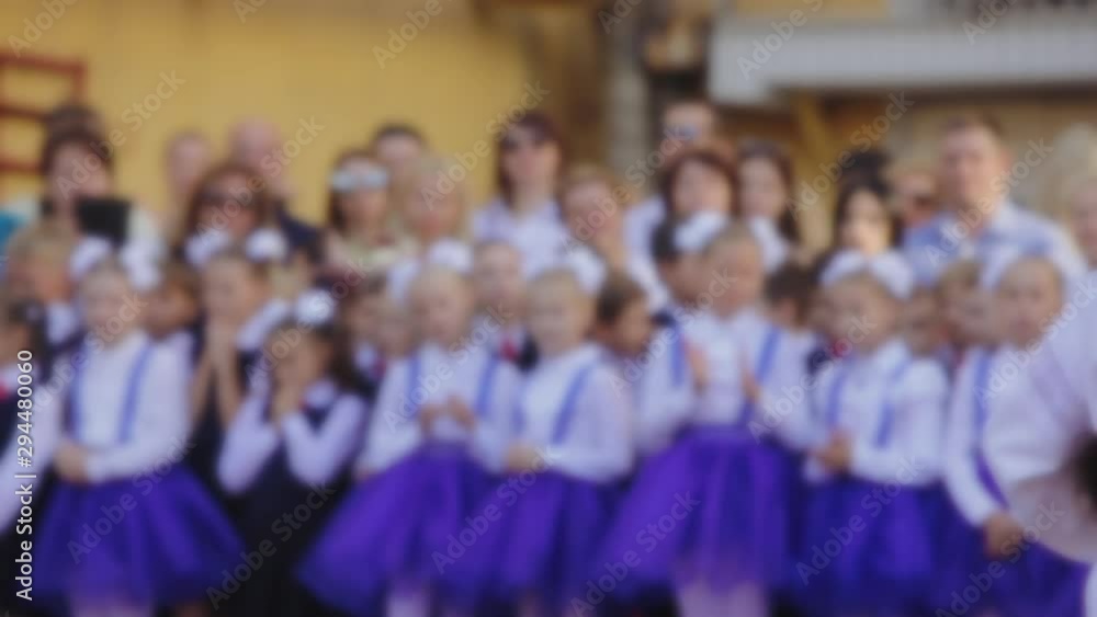 Girl in Ukrainian dress sings at the opening of the school year at school, blurred background of first graders, girls in blue dresses and white bows Girl in Ukrainian dress sings at the opening of the school year at school, blurred background of first graders, girls in blue dresses and white bows
