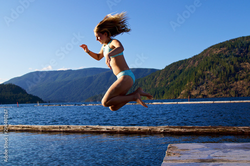 Carefree girl jumping off dock into sunny lake, Lake Cowichan, British Columbia, Canada photo