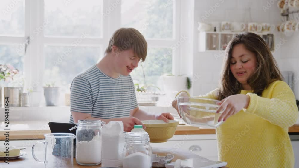 Young Downs Syndrome Couple Following Recipe On Digital Tablet To Bake Cake In Kitchen At Home Young Downs Syndrome Couple Following Recipe On Digital Tablet To Bake Cake In Kitchen At Home