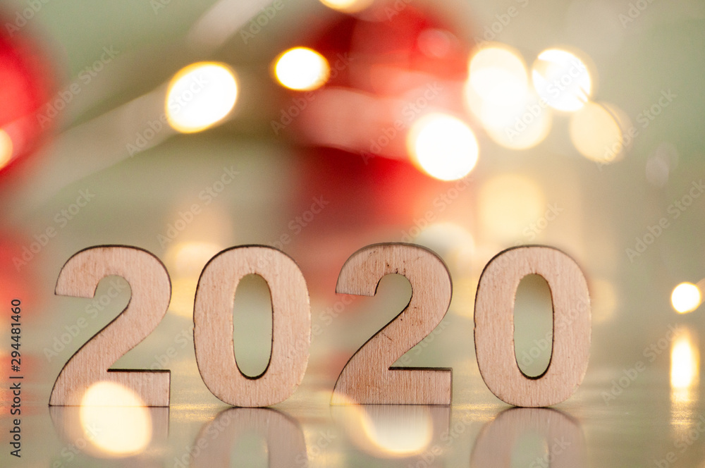 The inscription 2020, New Year and Christmas, from behind blurred dots of light on a blue background and red balls on the Christmas tree. Christmas and holiday. The inscription 2020, New Year and Christmas, from behind blurred dots of light on a blue background and red balls on the Christmas tree. Christmas and holiday.
