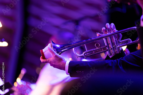 A musician playing a silver plated trumpet with one hand and with the other holding a cup mute inside the trumpet bell during a big band jazz concert