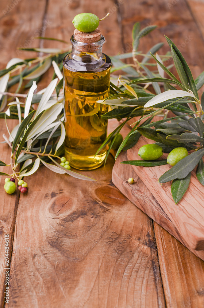 Bottle pouring virgin olive oil in a bowl close up. Fresh branches on a wooden background. Free space for text. Bottle pouring virgin olive oil in a bowl close up. Fresh branches on a wooden background. Free space for text.