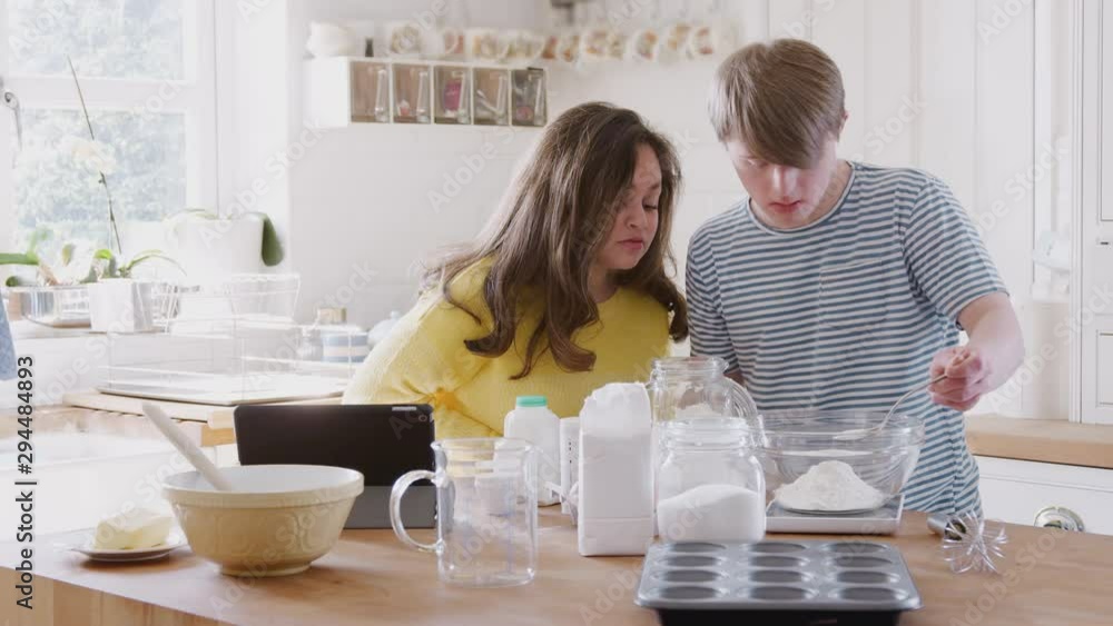 Young Downs Syndrome Couple Following Recipe On Digital Tablet To Bake Cake In Kitchen At Home Young Downs Syndrome Couple Following Recipe On Digital Tablet To Bake Cake In Kitchen At Home