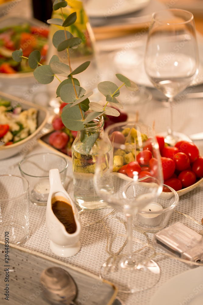 celebration, holidays, catering and eating concept - eucalyptus branch on table served with plates, wine glasses and food for home dinner party