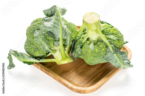 Group of two whole fresh green broccoli on wooden square plate isolated on white background photo