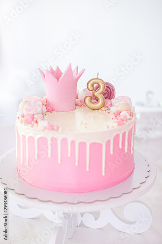 Happy birthday pink and white cake with marshmellows and a crown and with the number three on a white background.
