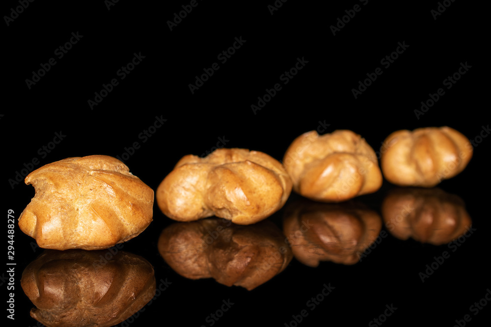 Group of four whole baked golden profiterole in row isolated on black glass