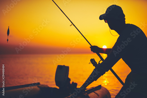 Silhouette of a fisherman fishing in sunset time on the open sea.