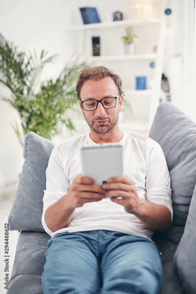 Man using tablet and sufring on the internet in his living room. Man using tablet and sufring on the internet in his living room.
