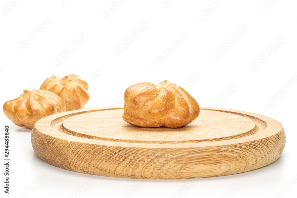Group of three whole baked golden profiterole one in focus on bamboo plate isolated on white background